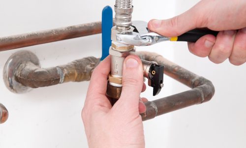 Hands repairing the plumbing pipes of an electric boiler with a spanner